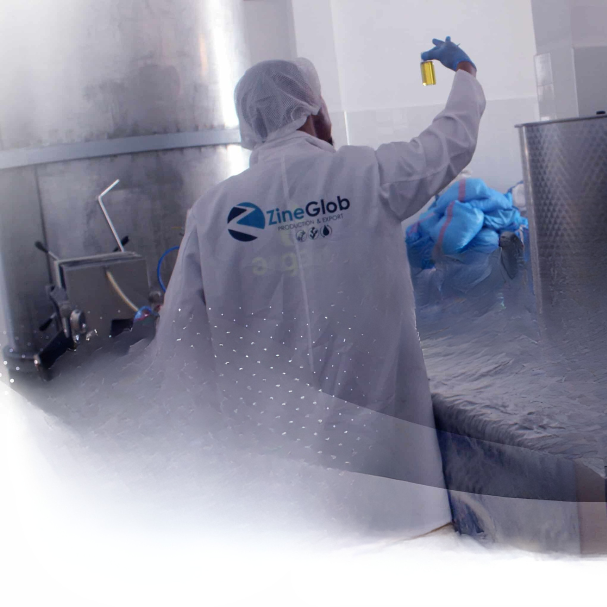 A quality control expert at ZineGlob factory holding up a glass vial to inspect the purity and golden color of premium Moroccan argan oil.